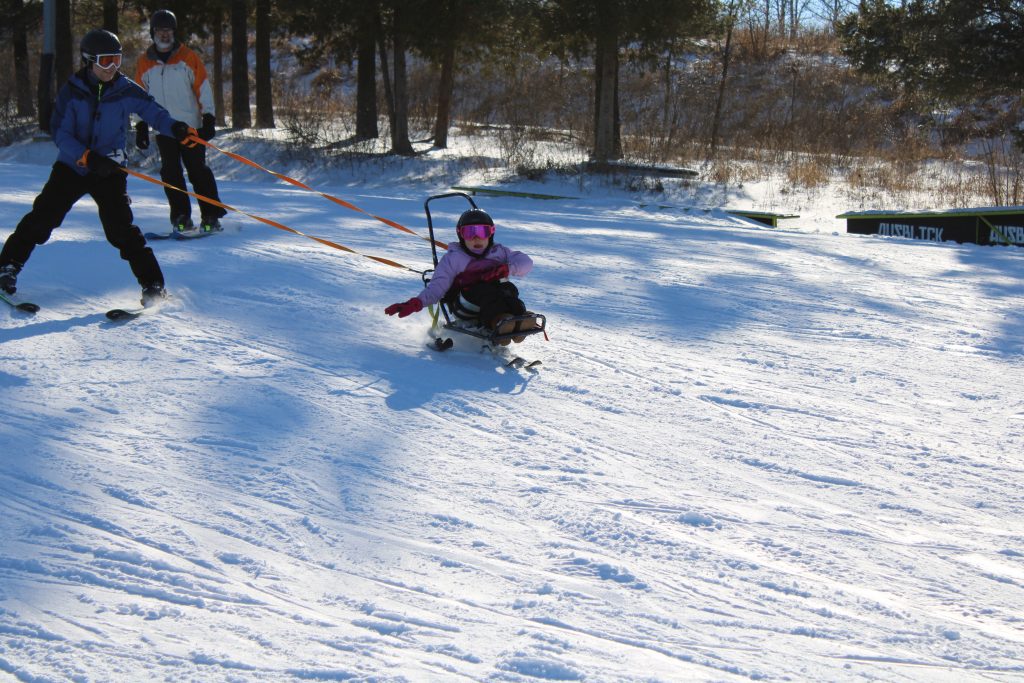 action photo of youth bi-skier skiing with the assistance of a volunteer