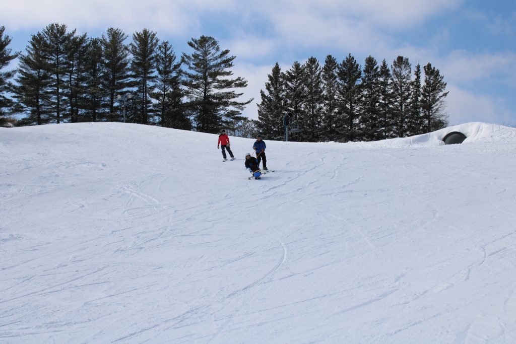 wide angle photo of student bi-skiing and coming down hill with assistance of instructors