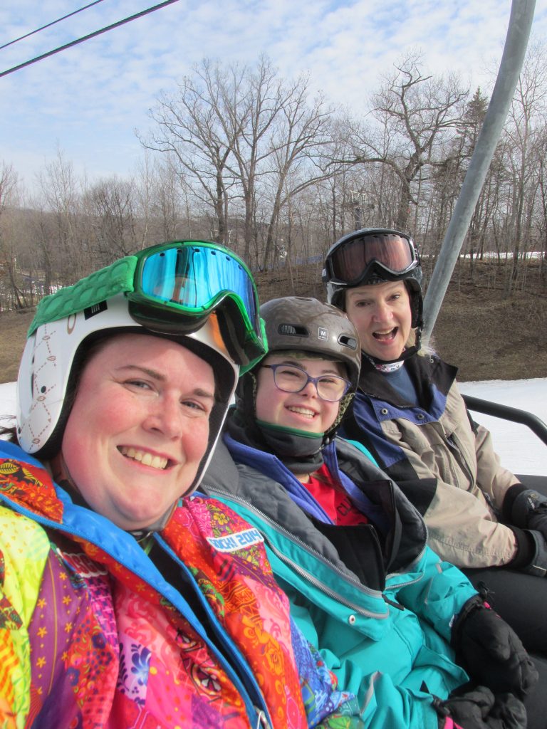 smiling volunteers and student riding up on a chairlift